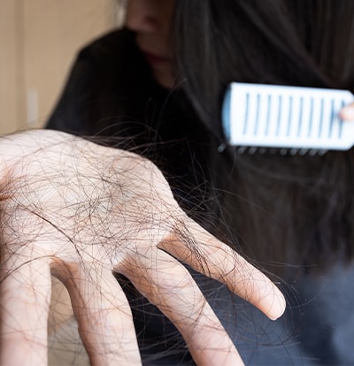 Hand mit vielen ausgefallenen Haaren nach dem Kämmen, Bürste im Hintergrund
