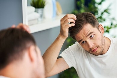 Un jeune homme regarde ses cheveux dans le miroir