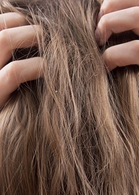 Frau mit langen, dunkelblonden Haaren von hinten kratzt sich an der Kopfhaut