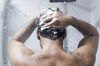 Mann von hinten steht in der Dusche und wäscht seine Haare