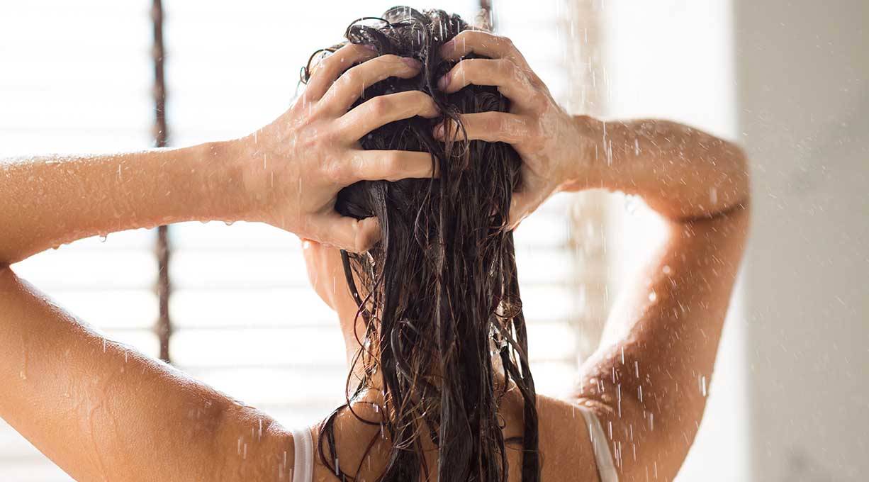 Rückenansicht einer Frau, die ihre langen, dunklen Haare mit trockenen Schuppen wäscht