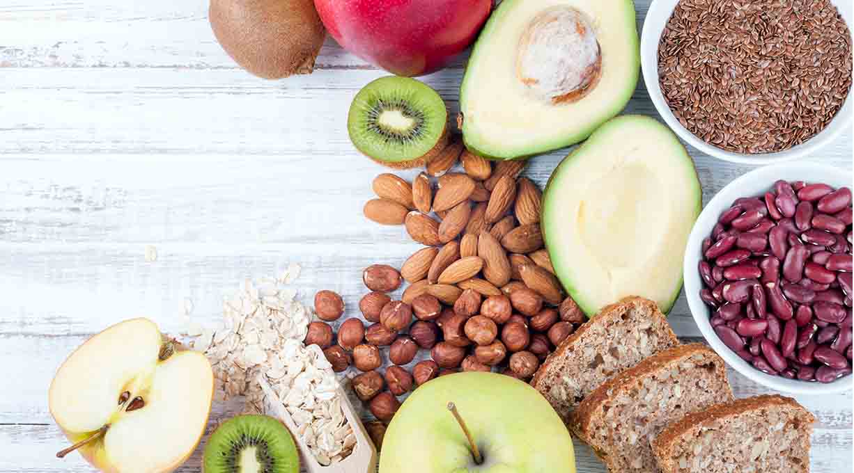 Eine Auswahl an gesunden Lebensmitteln gegen trockene Schuppen wie Äpfel, Nüsse, Kiwi und Vollkornbrot