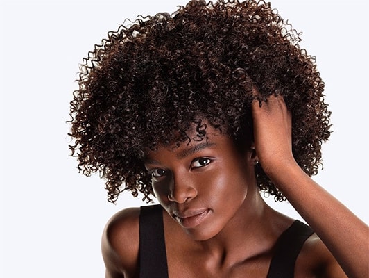 Nahaufnahme eines dunkelhaarigen, weiblichen Models mit Locken, das sich in die Haare greift