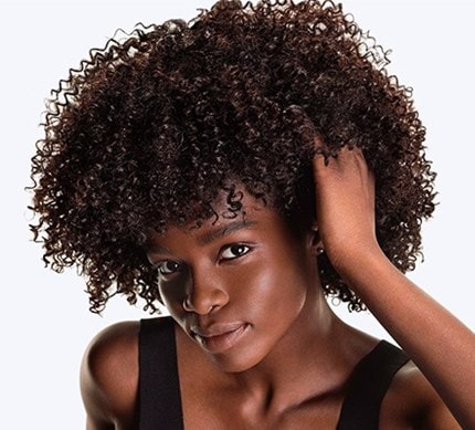 Nahaufnahme eines dunkelhaarigen, weiblichen Models mit Locken, das sich in die Haare greift