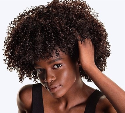 Gros plan d’un modèle féminin aux cheveux foncés et bouclés, passant la main dans ses cheveux.