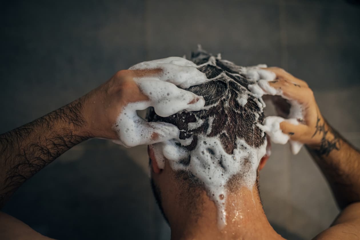 Mann wäscht seine Haare mit Shampoo unter der Dusch