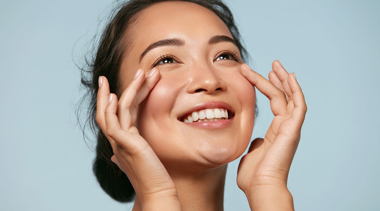 Junge Frau mit dunklen Haaren lächelt und berührt ihre Wangen