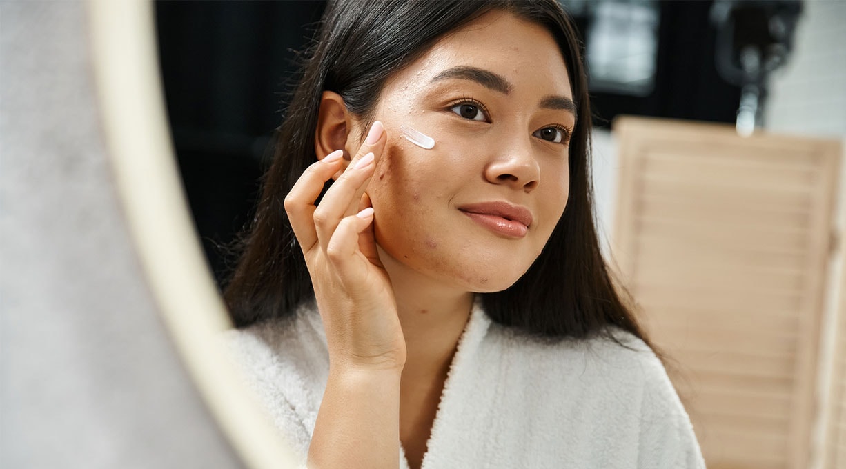 Une femme regarde sur le côté et s’applique de la crème sur le visage.
