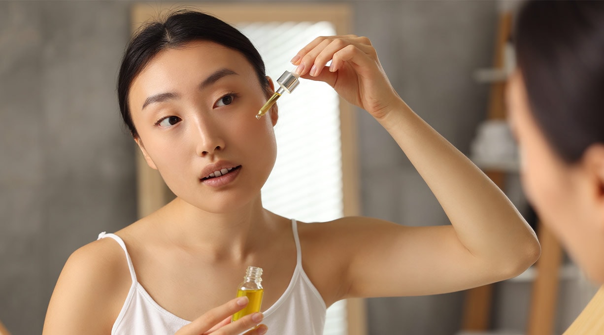Une femme se regarde dans le miroir et applique un sérum sur son visage.