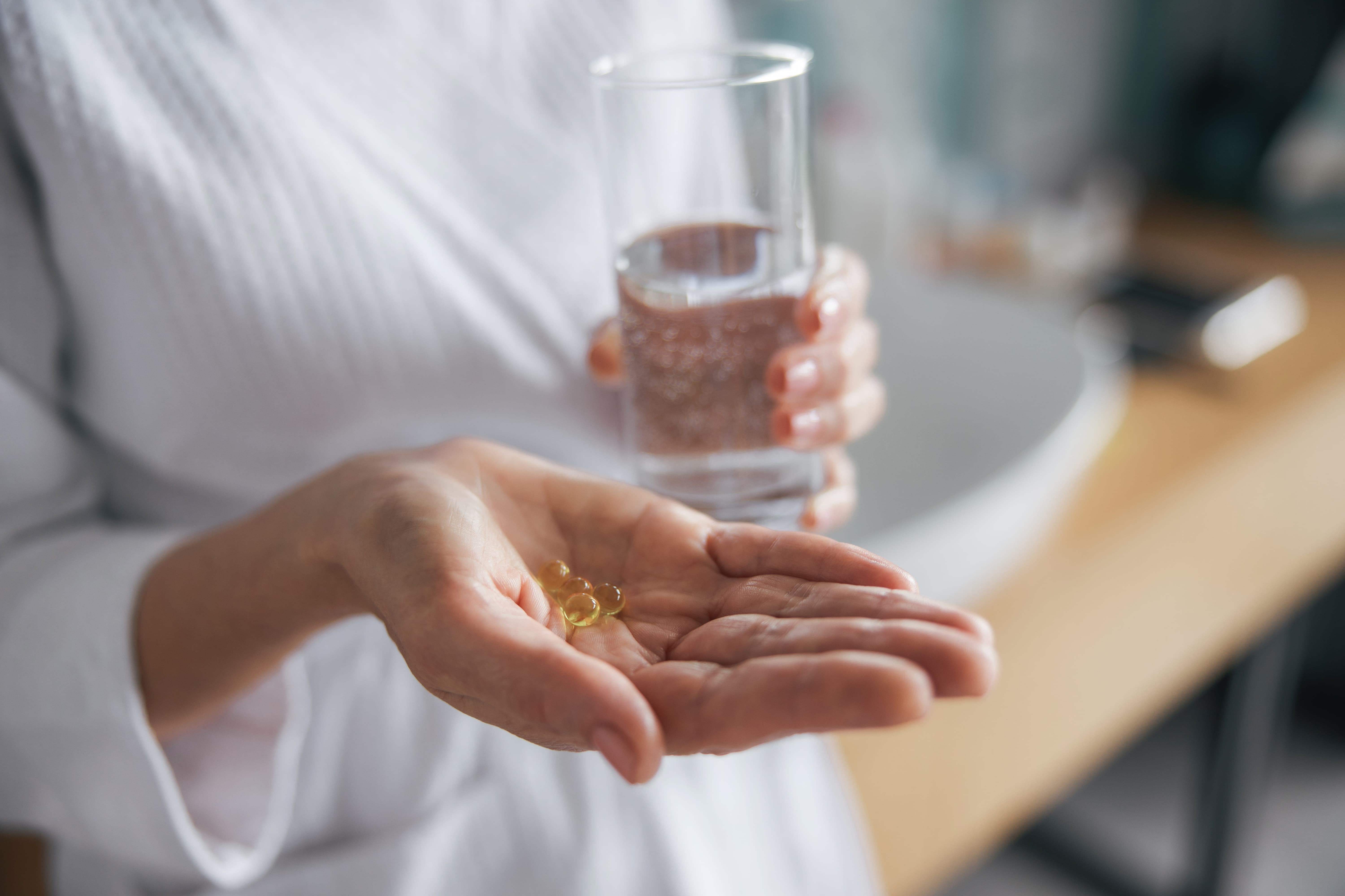 Person hält Nahrungsergänzungskapseln in der Hand und ein Glas Wasser