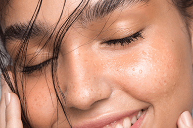 Femme souriante aux cheveux noirs avec une peau bien hydratée grâce au squalane
