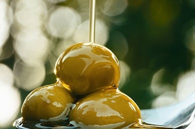 De l'huile d'olive coule sur plusieurs olives vertes superposées dans une cuillère