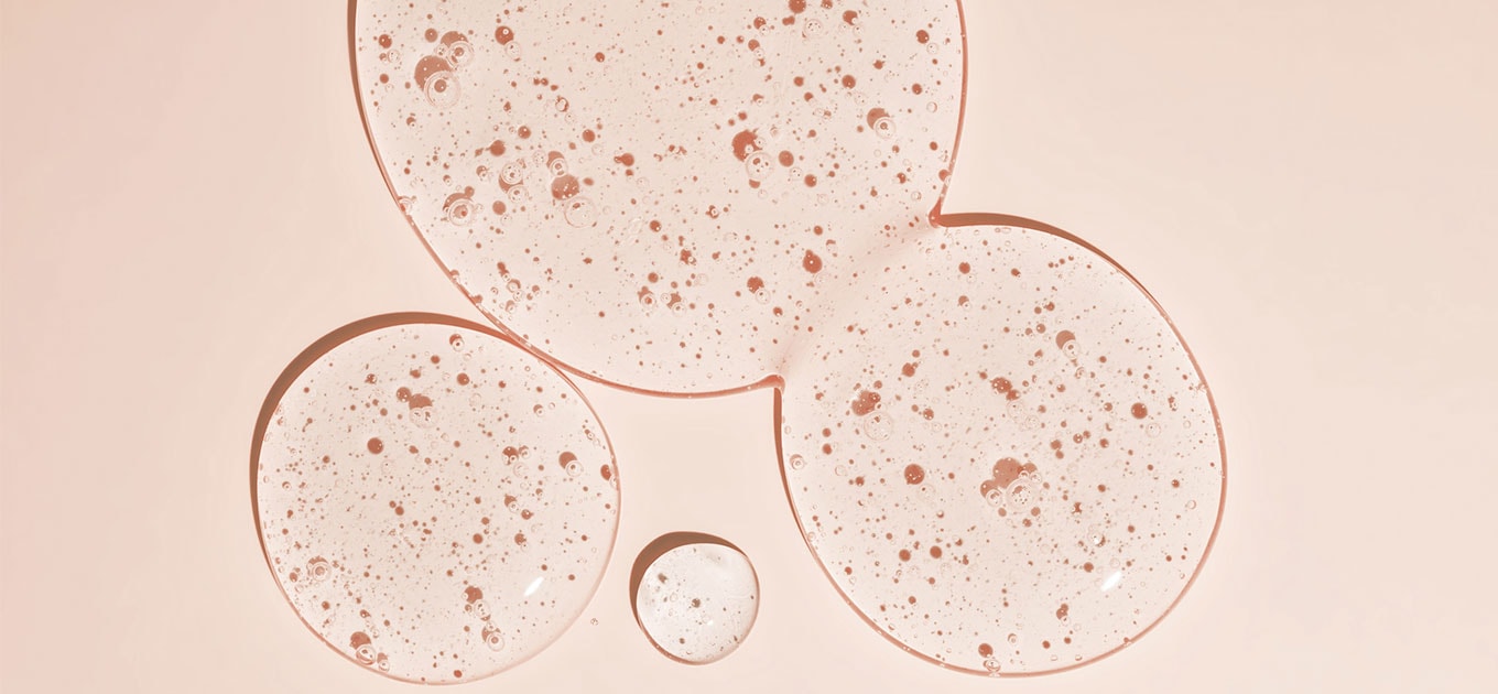 Ein paar Tropfen Squalan auf einem apricotfarbenen Untergrund