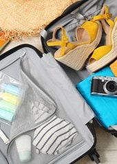 Geöffneter Koffer mit Sommerkleidung, Sandalen, Sonnenbrille und Reiseaccessoires für den Urlaub