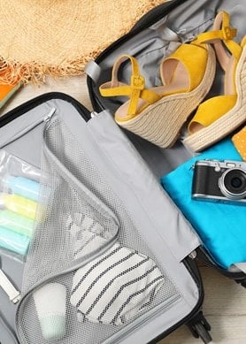 Geöffneter Koffer mit Sommerkleidung, Sandalen, Sonnenbrille und Reiseaccessoires für den Urlaub