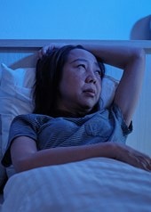Une femme reste éveillée la nuit dans son lit à cause de sueurs nocturnes, aux côtés d'un enfant endormi
