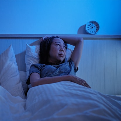 Frau liegt nachts wach im Bett wegen Nachtschweiss neben einem schlafenden Kind