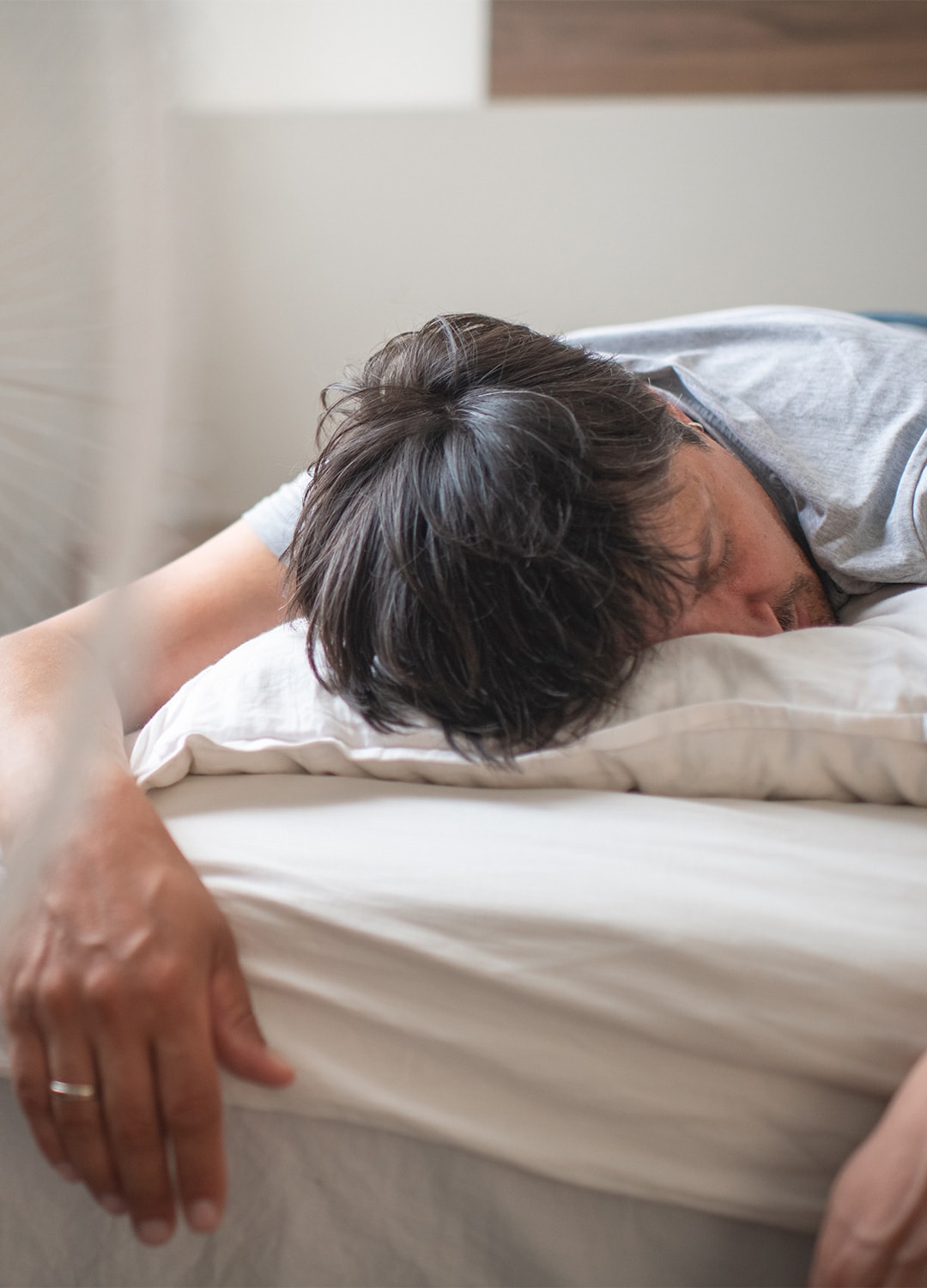 Mann liegt erschöpft auf einem Bett, während neben ihm ein Ventilator steht