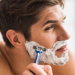 Un homme se rase la barbe avec de la mousse à raser et un rasoir à lames.