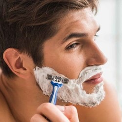 Un homme se rase la barbe avec de la mousse à raser et un rasoir à lames.