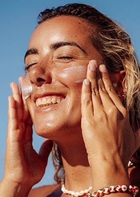Frau cremt ihr Gesicht in der Sonne ein, blauer Himmel im Hintergrund