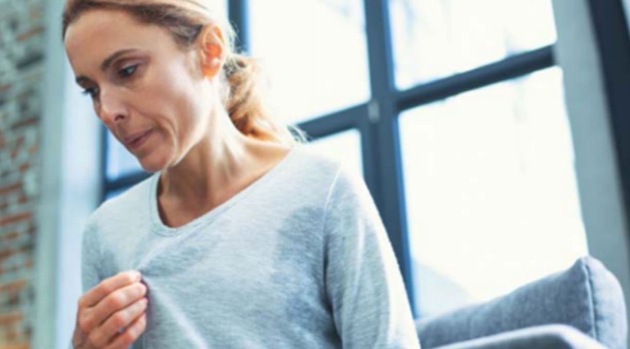 Eine Frau mit Hitzewallungen in den Wechseljahren sitzt auf dem Sofa und erholt sich. 
