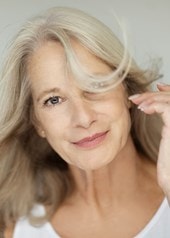 Frau mittleren Alters mit einem sanften Lächeln und graublonden Haaren, die ihr um das Gesicht wehen