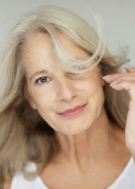 Frau mittleren Alters mit einem sanften Lächeln und graublonden Haaren, die ihr um das Gesicht wehen