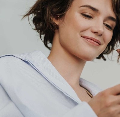 Une femme aux cheveux bruns courts regarde son téléphone en souriant