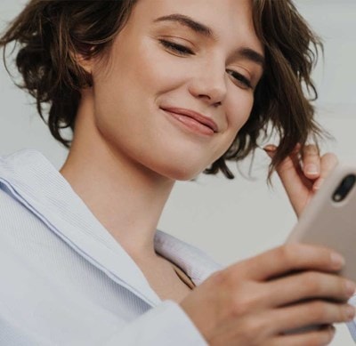 Person in weissem Hemd hält ein Smartphone in der Hand und berührt mit der anderen Hand eine Haarsträhne.