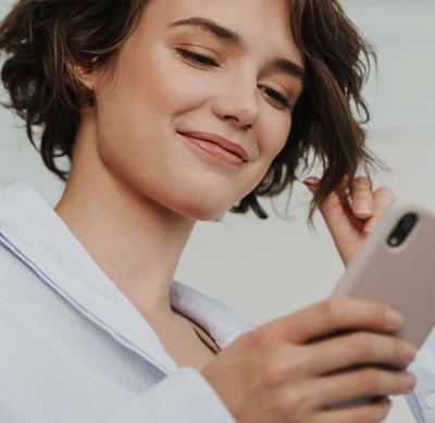 Person in weissem Hemd hält ein Smartphone in der Hand und berührt mit der anderen Hand eine Haarsträhne.
