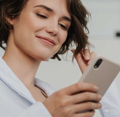 Person in weissem Hemd hält ein Smartphone in der Hand und berührt mit der anderen Hand eine Haarsträhne.