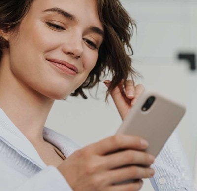 Person in weissem Hemd hält ein Smartphone in der Hand und berührt mit der anderen Hand eine Haarsträhne.