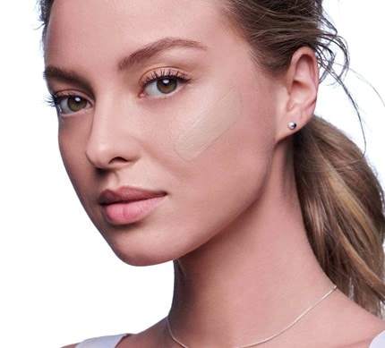 Frau mit lockigem, dunkelblongen Haaren schaut seitlich in die Kamera und hat auf ihrem Wangenknochen die VICHY Dermablend Foundation aufgetragen.