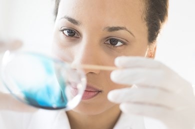 Une personne dans un laboratoire tient une boîte de Pétri contenant un liquide bleu, entourée d'un environnement baigné de lumière.