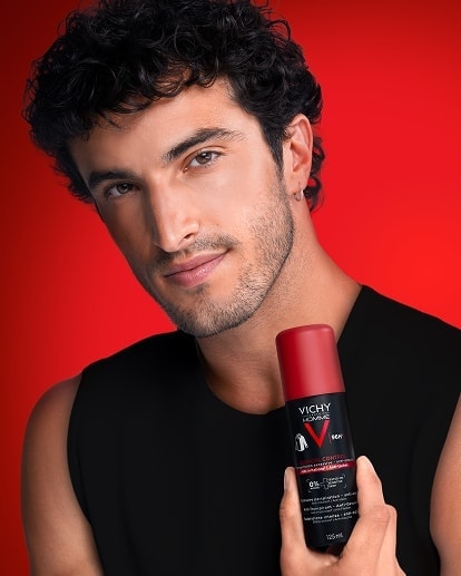 Mann hält Vichy Clinical Control Deodorant-Spray vor rotem Hintergrund