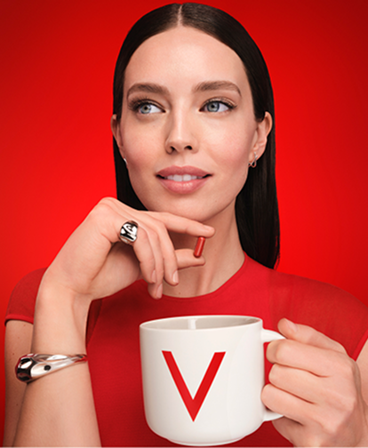 Frau in rotem Outfit hält eine weiße Tasse mit Vichy-Logo vor rotem Hintergrund