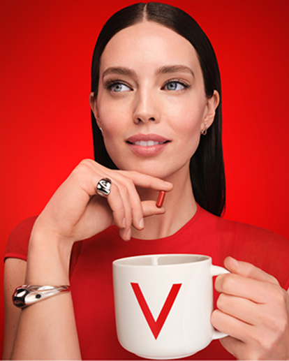 Frau in rotem Outfit hält eine weiße Tasse mit Vichy-Logo vor rotem Hintergrund