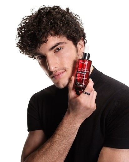 Junger Mann hält Vichy DERCOS R.E.G.E.N.-Flakon an seine Wange