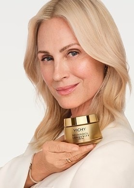 Blonde Frau hält einen goldenen Tiegel Vichy NEOVADIOL Longevity Cream