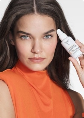 Frau mit orangenem Shirt hält Vichy UV Age Daily Sonnencreme in der Hand