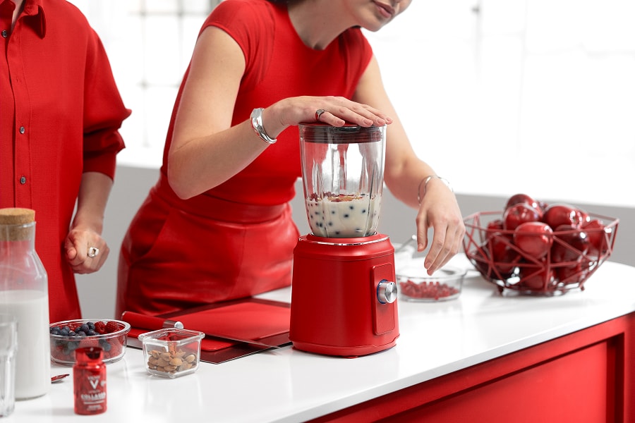 Gros plan d’une jeune femme en robe rouge en train de préparer un smoothie