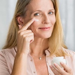 lächelnde Frau mittleren Alters trägt Creme auf ihre Wange auf
