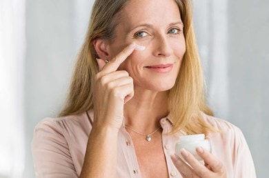 Une femme d'âge moyen souriante applique de la crème sur sa joue.