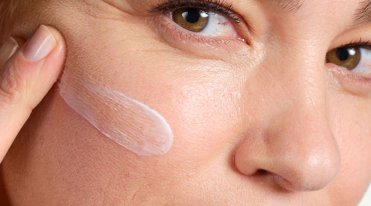 Application d'une crème pour visage sur la joue droite d'une femme.