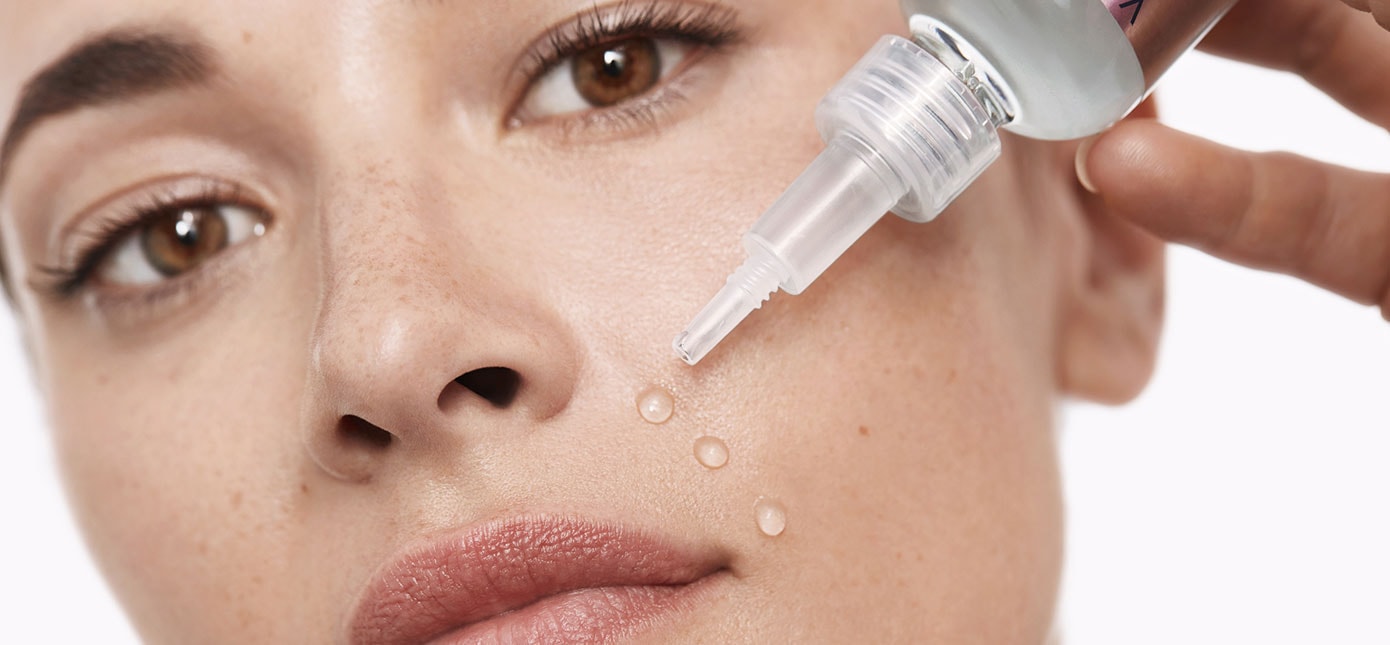 Junge Frau gibt drei Tropfen eines transparenten Serums auf die Haut um ihre Mundpartie