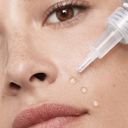 Junge Frau gibt drei Tropfen eines transparenten Serums auf die Haut um ihre Mundpartie