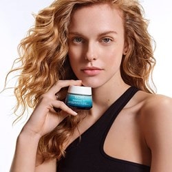Une femme tient le pot de crème MINÉRAL 89 100H Hydratation Boost dans sa main. Son visage est visible en arrière-plan