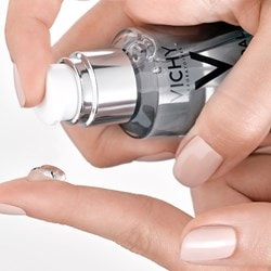 Hand hält ein Serum von Vichy und gibt einen Tropfen davon zur Anwendung auf den Finger