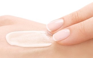 Zwei Finger verstreichen eine weisse Creme auf der Haut